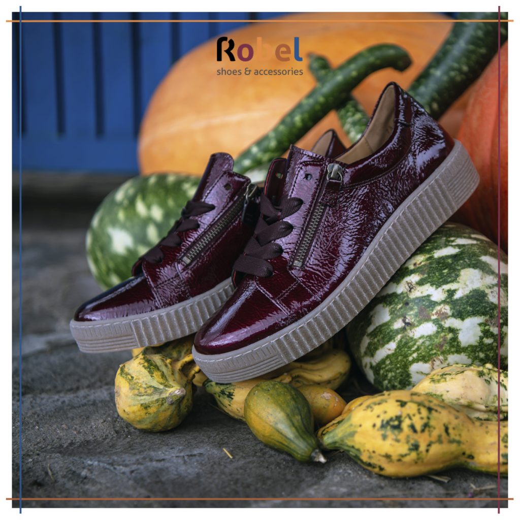 Lesklé bordové dámske tenisky so zipsom a hrubou podrážkou položené medzi tekvicami a okrasnými dyňami. Logo Robel shoes & accessories v hornej časti obrázka.